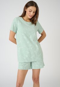 Lichtgroene loungewear set met een textuurachtig bloemenpatroon, bestaande uit een T-shirt met korte mouwen en bijpassende shorts. Zacht materiaal met een ontspannen pasvorm.