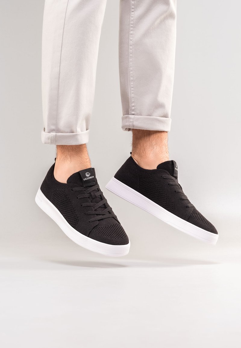 Schwarze Mesh-Sneaker mit weißen Gummisohlen, runder Zehenform, Schnürdesign und gepolstertem Kragen für zusätzlichen Komfort.