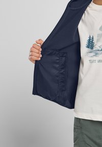 Navy fleece jacket with zippered pocket inside, featuring a smooth texture and contrasting lining. Worn over a light-colored t-shirt.