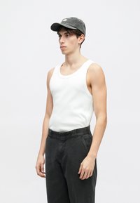 Biała bawełniana koszulka na ramiączkach o żebrowej fakturze w połączeniu z luźnymi, ciemnoszarymi spodniami. Na głowie noszona jest ciemnoszara czapka z logo.