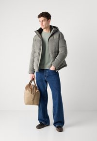 Grå pufferjakke med kordfløjl og glatte paneler; grøn sweater; blå vide jeans; brun taske med læderdetaljer; sorte sko.