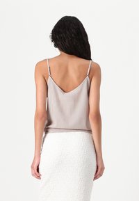 Top de tirantes finos en rosa claro con diseño de espalda en V, combinado con una falda blanca texturizada. Silueta minimalista y ajustada.