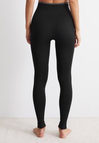 Černé legíny s texturovaným vzorem, vysokým pasem a přiléhavým střihem, zúžené u kotníků. Tkanina vypadá elasticky a hladce.
