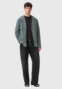 Miętowy, puszysty kardigan o fakturowanym wykończeniu, zapinany z przodu, noszony na czarnej koszulce i zestawiony z luźnymi czarnymi dżinsami.