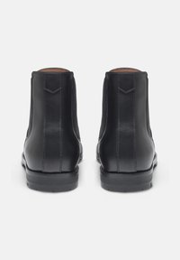 Stivaletti neri in pelle con una texture liscia, pannelli elastici laterali e suola in gomma resistente. Presentano cuciture minimali e un tab posteriore per l'estrazione.