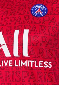 Camiseta roja del Paris Saint-Germain con el texto "PARIS" repetido, el logo del club y la inscripción blanca "ALL LIVE LIMITLESS" como patrocinio.