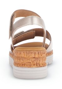 Metallisch-beige Sandale mit drei verstellbaren Riemen und einer strukturierten Korkplattformsohle. Die weiße Gummibasis verbessert Stabilität und Komfort.