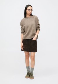 Pull en tricot marron à manches longues, assorti à une jupe en daim marron foncé avec deux poches avant. Des chaussettes vertes et des baskets complètent le look.