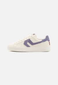 White sneaker featuring a soft purple suede accent, flat laces, a textured rubber sole, and a small red and white logo patch on the tongue.