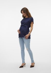 Šaljna plava bluzica s mašnom u struku, uparena s svijetloplavim iscepanim skinny trapericama i smeškim štiklama s dekorativnim detaljima.