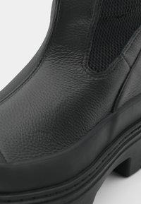 Stivale alla caviglia nero con tomaia in pelle textured e pannelli laterali in rete, caratterizzato da una suola in gomma spessa e dettagli di cucitura discreti.