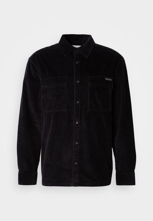 Sort corduroy skjorte med knaplukning foran, to brystlommer og klassisk krave. Tekstureret stof med lodrette ribber.