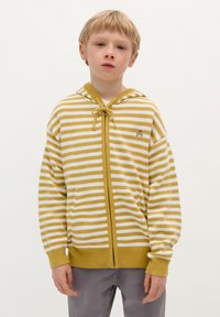 Sweat à capuche rayé jaune et blanc avec une fermeture éclair sur le devant, une capuche avec cordon de serrage et des poignets côtelés. Petit logo de crâne sur la poitrine gauche.