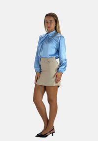 Blusa di raso blu chiaro con maniche a palloncino, abbinata a una gonna beige a vita alta. Le décolleté nere a punta completano l'outfit.