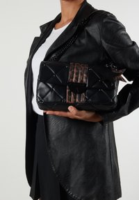 Kuitutettu musta nahkakäsilaukku, jossa on leopardikuosiset yksityiskohdat ja ketjuhihna. Laukussa on tähden muotoinen metallikoriste ja lukitus.