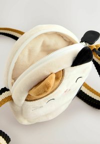 Runde Plüsch-Tasche mit cremefarbenem Fleece, die ein lächelndes Gesicht zeigt, braune Ohrenakzente und einen Reißverschluss hat. Gestreifter Gurt in Gelb und Schwarz.