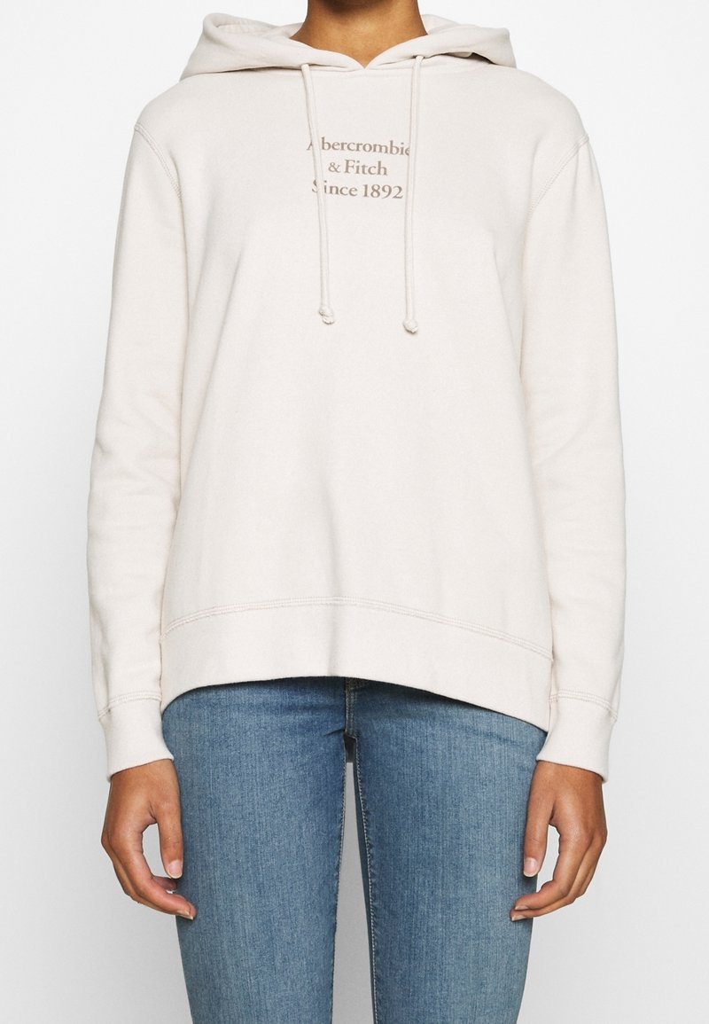 Hellbeiger Hoodie aus weichem Stoff mit einer vorderen Kängurutasche, verstellbaren Zugbändern und bedrucktem Logo-Text. Lockerer Schnitt.