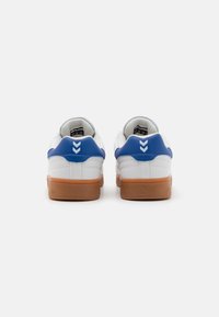 Fehér sneakers kék díszítéssel, gumis talppal. A hátsó részen egy logó és két kék, chevron-szerű minta található.