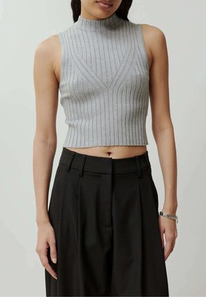 Kobieta ubrana w bezrękawną, prążkowaną szarą crop top i czarne spodnie z wysokim stanem, z srebrną bransoletką na prawej ręce.
