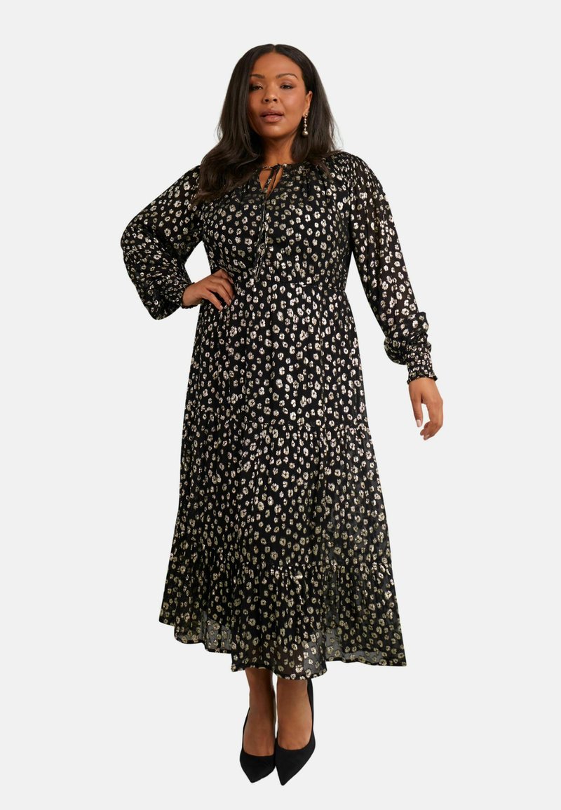 Svart maxiklänning med vitt och guld blommönster, genomskinlig tyg, långa puffärmar, lager på lager-kant och justerbar knytning i halsen.