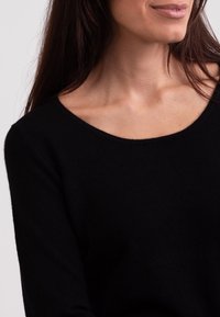 Schwarzer Wollpullover mit weitem Ausschnitt und langen Ärmeln, der eine glatte Textur und minimale Nähte aufweist. Fokus auf den Bereich des Oberkörpers.