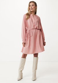 Abito lungo rosa a maniche lunghe con colletto, vita stretta e tessuto testurizzato. Abbinato a stivali bianchi fino al ginocchio. Fit semplice e rilassato.