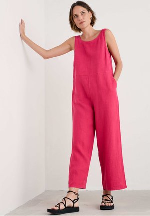 Rosa Leinen-Overall mit lockerer Passform, ärmellosem Design und seitlichen Taschen; mit Knopfakzenten an den Schultern und kombiniert mit schwarzen Riemchensandalen.