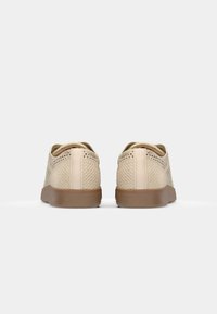 Paire de chaussures décontractées beige texturées avec semelles marron vues de dos sur un fond blanc.