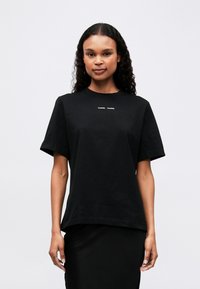 Black cotton t-shirt with short sleeves, round neckline, and a subtle white logo on the chest. Relaxed fit; smooth texture.