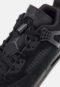 Gros plan d'une basket Air Jordan noire montrant des lacets texturés, le logo Jumpman sur la languette et des détails perforés sur le panneau latéral.