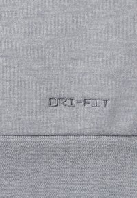 Szary materiał Dri-FIT o teksturowanym splocie, z haftowanym logo "DRI-FIT". Gładka powierzchnia z delikatnym połyskiem i miękkim wykończeniem.