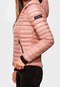 Różowa kurtka z ociepleniem, z poziomymi przeszyciami, zapinanymi na zamek kieszeniami oraz czarną łatą z logo na ramieniu. Posiada kaptur i ściągacze przy mankietach.