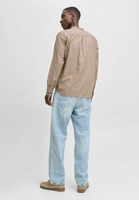 Brown long-sleeve shirt with a button-down collar, paired with light blue denim jeans. The fabric is smooth with a subtle texture.