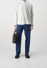 Weißes Langarmhemd mit Stehkragen, blaue Jeans aus Denim, schwarze strukturierte Handtasche und schwarze Plateaustiefel. Schlichte, lässige Kleidung.