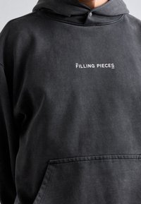 Sudadera negra de mezcla de algodón, con un bolsillo frontal y el logotipo blanco de "Filling Pieces". Textura suave con un corte relajado.