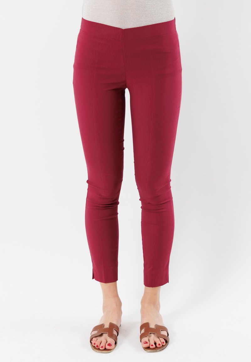 Leggings stretch bordeaux con un design aderente e taglio alla caviglia. Texture liscia con una leggera lucentezza, abbinati a sandali scivolosi marroni.