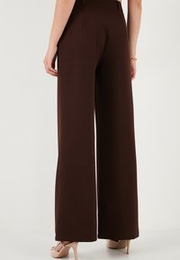 Braune, weit geschnittene Hosen aus glattem Stoff mit hohem Bund. Von hinten gesehen, mit feinen Nähten und ohne sichtbare Taschen.