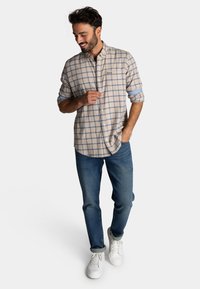 Lichtbeige geruit shirt met blauwe lijnen, met knoopsluiting, opgerolde mouwen, gecombineerd met blauwe spijkerbroek en witte sneakers.