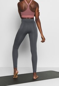 Grå högmidjade leggings och en ribbad rosa sportbehå med racerback-design. Tyget verkar glatt och elastiskt.