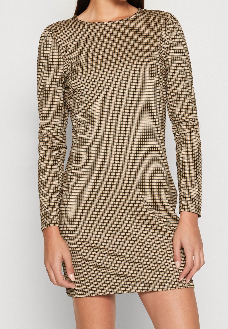 Robe mini à manches longues en tissu texturé avec un motif à carreaux beige et noir, présentant un col rond et une silhouette ajustée.
