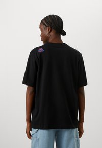 Black cotton t-shirt with short sleeves and a crew neck. Features a colorful embroidered detail on the upper back. Smooth texture.