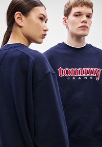 Tmavomodré mikiny z bavlnenej zmesi s výrazným červeno-bielym logom "Tommy Jeans" na prednej strane. Príležitostný strih, rebrované manžety.