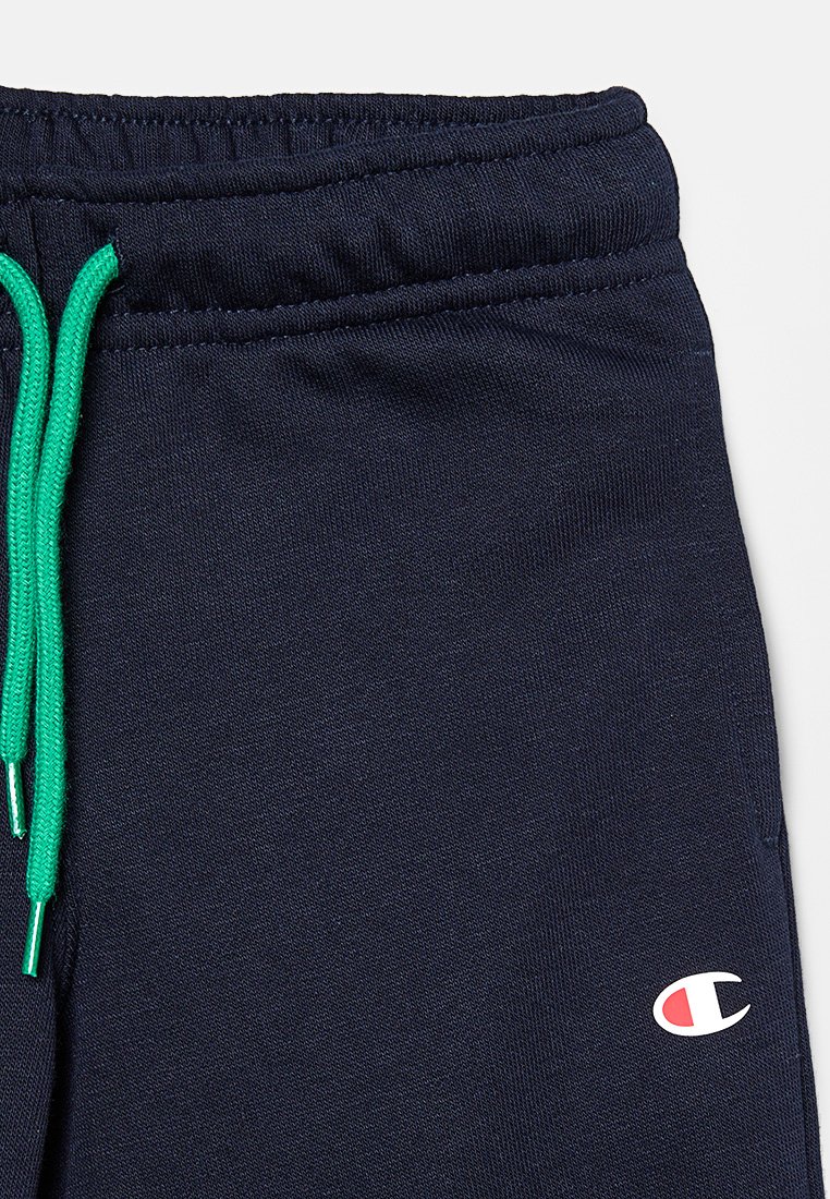 Pantalons de survêtement navy avec taille à cordon de serrage et accents verts, fabriqués en tissu doux, affichant un petit logo rouge en bas à gauche.