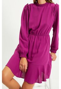 Robe violette à manches longues, détails à volants sur les épaules, taille élastique et ourlet évasé. Confectionnée dans un tissu lisse.