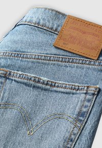 Světle modré džíny z denimu s koženou značkovou nášivkou na pásku. Obsahují kontrastní stehy a klasický design zadních kapes.