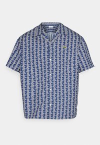 Košile s krátkým rukávem v modré barvě s bílým geometrickým vzorem. Na levé hrudi má malé logo, vyrobená z lehkého materiálu.