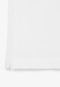 Tissu blanc à tissage texturé, avec un ourlet cousu et un détail de fente latérale.