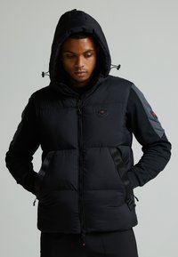 Μαύρο μπουφάν με κουκούλα, διαθέτει πλισέ υφή, λογότυπο στη θωράκιση, τσέπες με φερμουάρ και αντίθετους γκρίζους μανίκους.