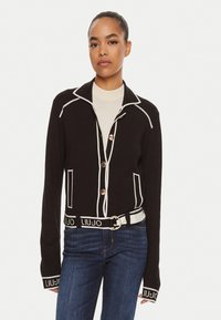 Cardigan nero con rifiniture bianche, dotato di colletto, bottoni e cintura con logo. Progettato con tasche frontali e una silhouette aderente.