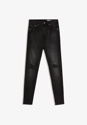 Black skinny jeans with distressed patches on both knees, five-pocket style, and copper rivet details, laid flat on white background.